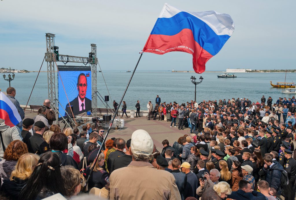 epa04170019 Crimean people watch a TV broadcast with Russian President Vladimir Putin speaking during his annual call-in live broadcast, on the seafront in Sevastopol, Crimea, 17 April 2014. The decision to send tanks and combat aircraft to eastern Ukraine is another serious crime committed by the authorities in Kiev, Putin said. He called on the Ukrainian government to engage in 'real dialogue' with its Russian-speaking population, adding that the deployment of 'military planes and tanks' would not solve the crisis in eastern Ukraine. In his televized call-in show Putin said that Kiev's decision to curb the protests in the eastern region of Donetsk with military force was a 'crime.'  EPA/ANTON PEDKO
