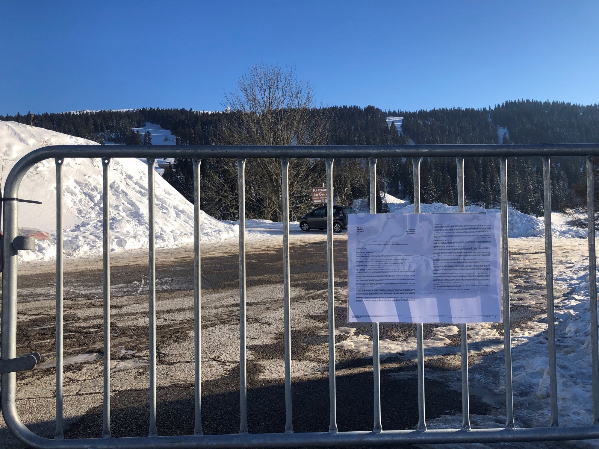 Des barrières vauban, sur lesquelles est affichée une copie du premier arrêté préfectoral du 29 décembre 2020, entravent l'accès au parking des Dappes, donc au domaine skiable suisse de la Dôle.