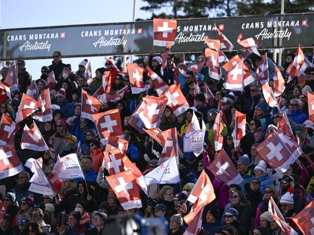 Spectators wave Swiss flags in the air at the finish area of the women's Downhill race at the FIS Alpine Ski World Cup in Crans-Montana, Switzerland, Sunday, February 27, 2022. (KEYSTONE/Jean-Christophe Bott)