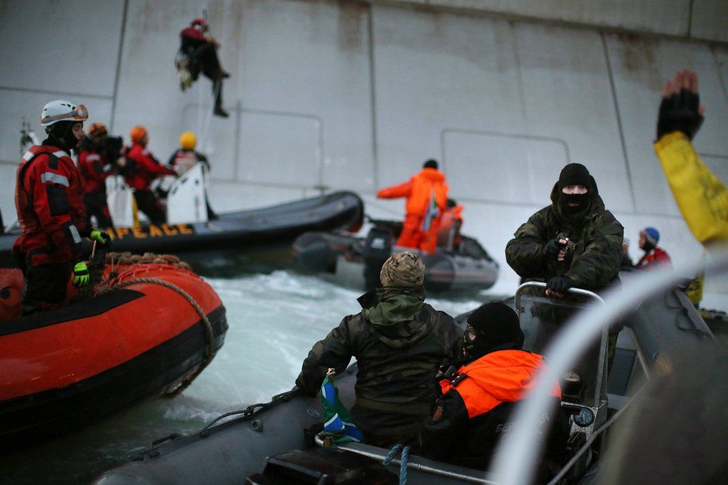 In this image released by environmental organization Greenpeace, a Russian Coast guard officer, right,  points a gun at a Greenpeace International activist, left in yellow uniform, as five activists attempt to climb the Prirazlomnaya, an oil platform operated by Russian state-owned energy giant Gazprom platform in Russia's Pechora Sea, a section of the Barents Sea, Wednesday, Sept. 18, 2013. Greenpeace said two of its activists have been arrested after climbing onto the oil platform in Russia's Arctic waters. The group claims warning shots were fired across the organization's ship.  (AP Photo/Greenpeace, Denis  Sinyakov)  NO RESALE, NO ARCHIVE