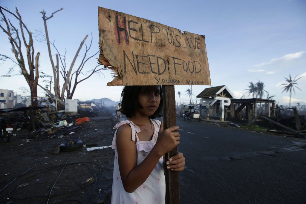 A typhoon survivor displays a placard with a message along a highway at typhoon-ravaged Palo township, Leyte province in central Philippines at sunrise Wednesday, Nov. 27, 2013. Typhoon Haiyan, one of the most powerful storms on record, hit the country's eastern seaboard Nov. 8, leaving a wide swath of destruction. (AP Photo/Bullit Marquez)