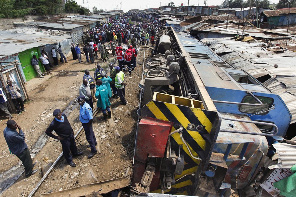 epa03998907 Police officers and rescue workers gather around an overturned freight train that crashed into homes built along the railway track in Kibera slum in Nairobi, Kenya, 22 December 2013. A freight train heading to Uganda derailed and crashed into homes as it was passing through one of the biggest slums in Africa, injuring several people. Several people are feared trapped underneath the wreckage, the Kenya Red Cross says. Workers are trying to straighten the railway track to make a way for a heavy machinery to come and haul an overturned train cars.  EPA/DAI KUROKAWA