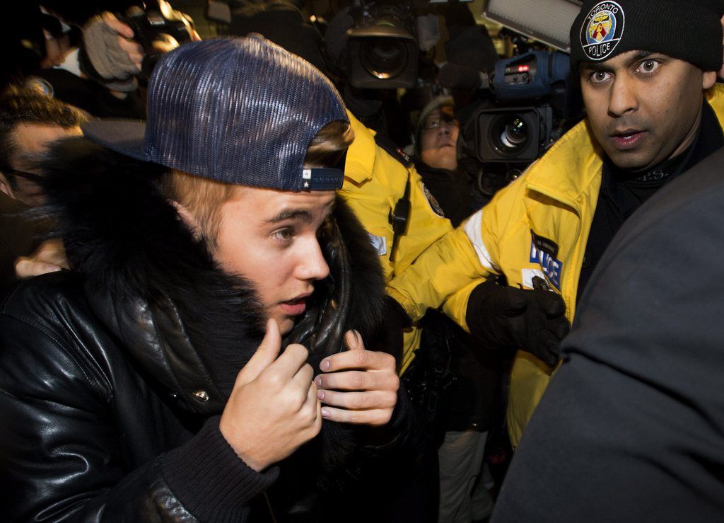 Canadian musician Justin Bieber is swarmed by media and police officers as he turns himself into city police for an expected assault charge, in Toronto, on Wednesday, Jan. 29, 2014. A police official said the charge has to do with an alleged assault on a limo driver in December. (AP Photo/The Canadian Press, Nathan Denette)