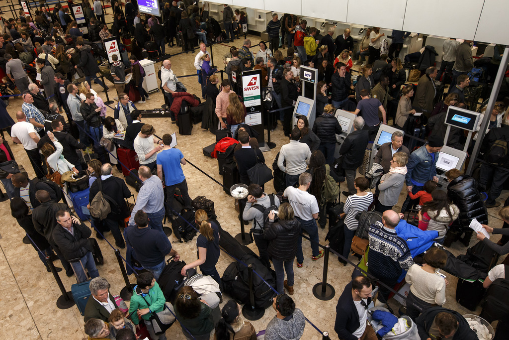 Des passagers attendent avec leurs bagages devant les guichets pour faire leurs check-in, à l'aéroport de Genève. 