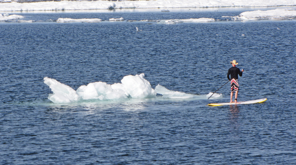 In this photo taken on Tuesday, May 27, 2014, a paddle boarder moves past a large piece of ice in Lake Superior in Marquette, Mich. The warmest temperatures of the year sent people to the Lake Superior shoreline, where small icebergs were abundant in the water, the final vestige of a bitterly cold winter. (AP Photo/The Mining Journal, Dave Schneider)