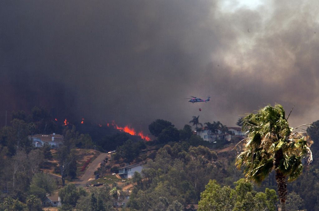 A helicopter files over San Marcos, Calif. on Thursday, May 15, 2014 as wildfires climb a hill eastward towards Mission Hills High School where the Red Cross has set up an evacuation center. The fires have come during a heat wave in the drought-stricken state. (AP Photo/UT San Diego, Peggy Peattie)
