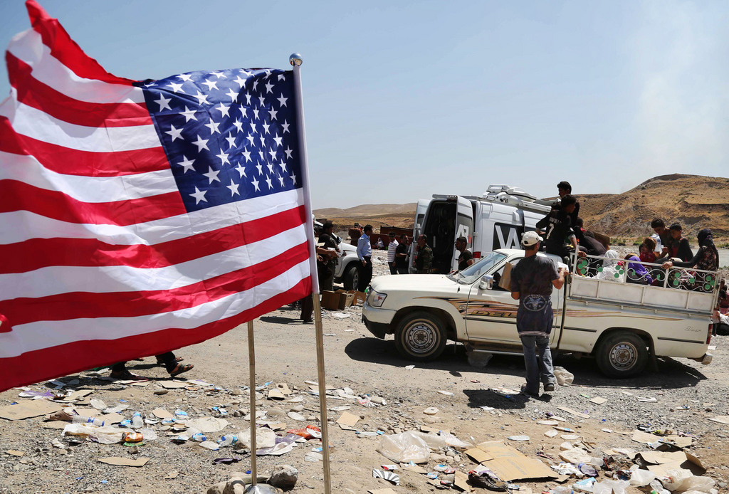 In this Sunday, Aug. 10, 2014 photo, a U.S. flag waves while displaced Iraqis from the Yazidi community cross the Syria-Iraq border on Feeshkhabour bridge over Tigris River at Feeshkhabour border point, northern Iraq. Kurdish authorities at the border believe some 45,000 Yazidis passed the river crossing in the past week and thousands more are still stranded in the mountains. (AP Photo/ Khalid Mohammed)