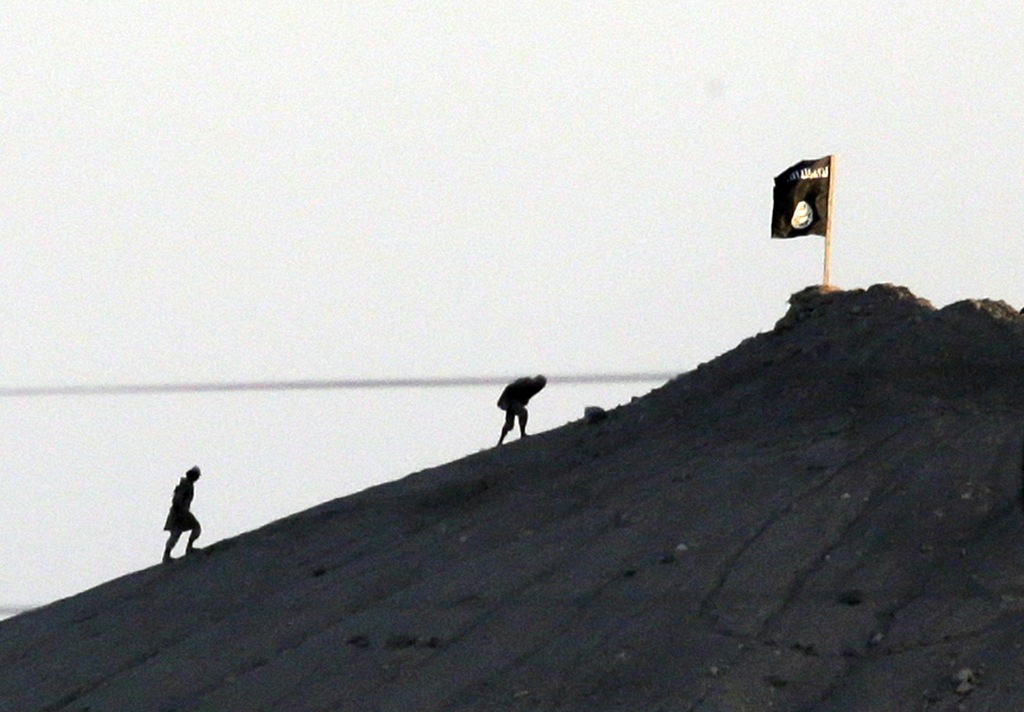 FILE In this Oct. 6, 2014 file photo,  shot with an extreme telephoto lens and through haze from the outskirts of Suruc at the Turkey-Syria border, militants with the Islamic State group are seen after placing their group's flag on a hilltop at the eastern side of the town of Kobani, Syria. After two months, the U.S.-led aerial campaign in Iraq has so far hardly dented the core of the Islamic State group?s territory. The extremists? grip on major cities across Iraq and neighboring Syria remains unquestioned. The campaign has brought some gains, with Kurdish fighters taking back towns on the fringes of the Islamic State group?s territory. But those successes only underline a major weakness: Besides the Iraqi Kurds, there are no forces on the ground ready to capitalize on the airstrikes. (AP Photo/Lefteris Pitarakis)