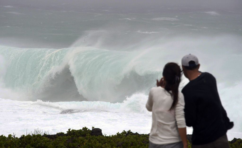 A couple watches huge wave at a cape in Yomitan Village, Japan's southern island of Okinawa Sunday, Oct. 12, 2014. A powerful typhoon poured heavy rains over Okinawa and was aiming at the next island of Kyushu on Sunday, becoming the second severe storm to hit in a week. (AP Photo/Kyodo News)  JAPAN OUT, MANDATORY CREDIT