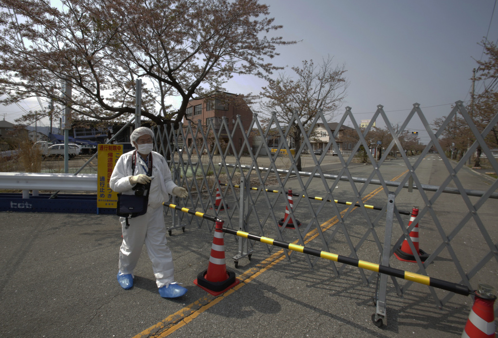 In this photo taken Thursday, April 17, 2014, Kazuhiro Onuki wearing a white protective gear and a filtered mask walks by a fence blocking the traffic in Tomioka, Fukushima Prefecture, northeastern Japan. The streets were abandoned, except for a car passing through, now and then. The neighborhood was eerily quiet except for the chirping of the nightingales. It?s difficult to imagine ever living again in Tomioka, a ghost town about 10 kilometers (6 miles) from the former Fukushima Dai-ichi nuclear plant. (AP Photo/Shizuo Kambayashi)