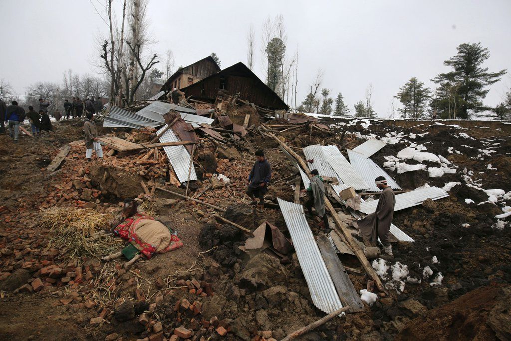epa04686446 Kashmiri villagers walk near damaged residential houses following a landslide due to heavy rainfall in the village of Laden at Chadoora some 40 kms west of Srinagar , the summer capital of Indian Kashmir, 30 March 2015. Rescuers are currently searching for the survivors underneath mud and debris of a residential house hit by the landslide in Laden village. Police says at least 16 people were buried under the debris.  EPA/FAROOQ KHAN