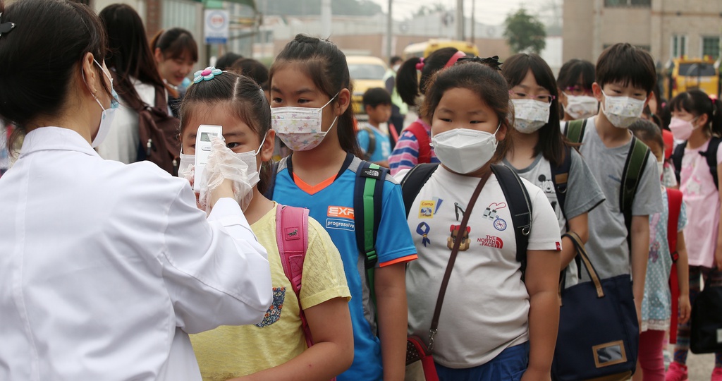 A health worker, left, checks the body heat of children wearing masks as a precaution against the Middle East Respiratory Syndrome (MERS) virus as their school reopened after it was temporarily closed at an elementary school in Pyeongtaek, South Korea, Monday, June 15, 2015. The outbreak of MERS has caused panic in South Korea.(Shin Young-geun/Yonhap via AP) KOREA OUT