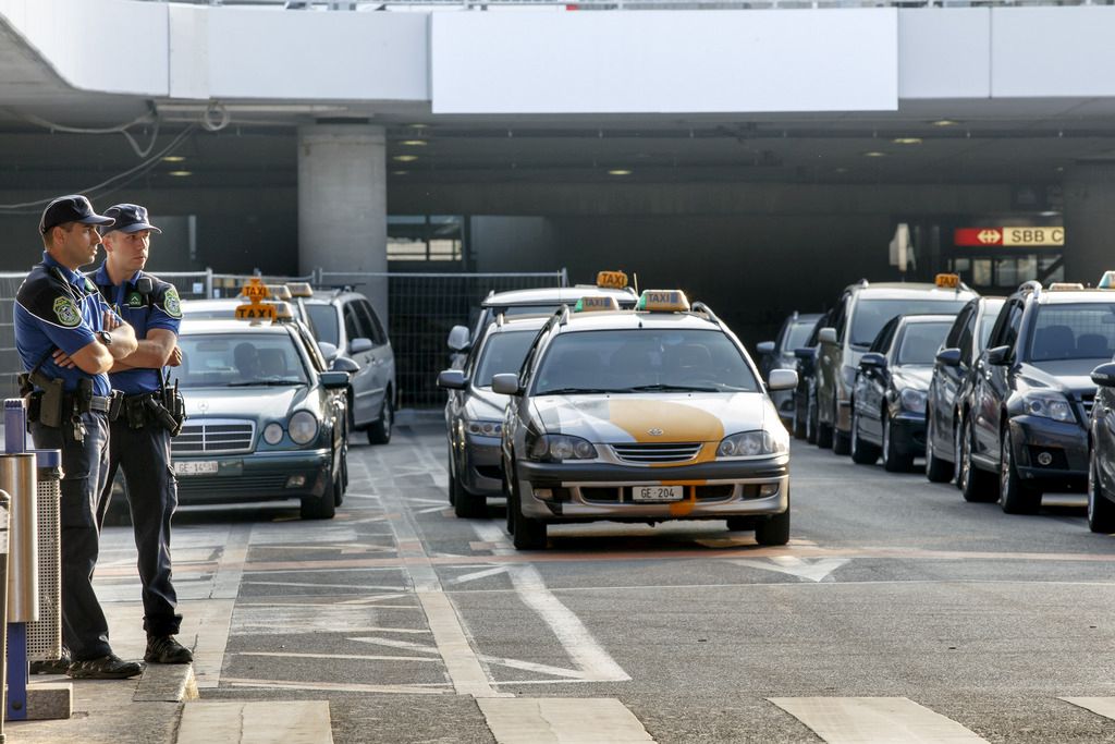 Deux policiers de la police genevoise sont en attentes vers la station de taxi de l'aeroport de Geneve pour prevenir tout mouvement de protestation, alors que des chauffeurs de taxis roulent en cortege sur quai du General Guisan pour protester contre Uber et l'Etat de Geneve, ce lundi, 6 juillet 2015, a Geneve. (KEYSTONE/Salvatore Di Nolfi)