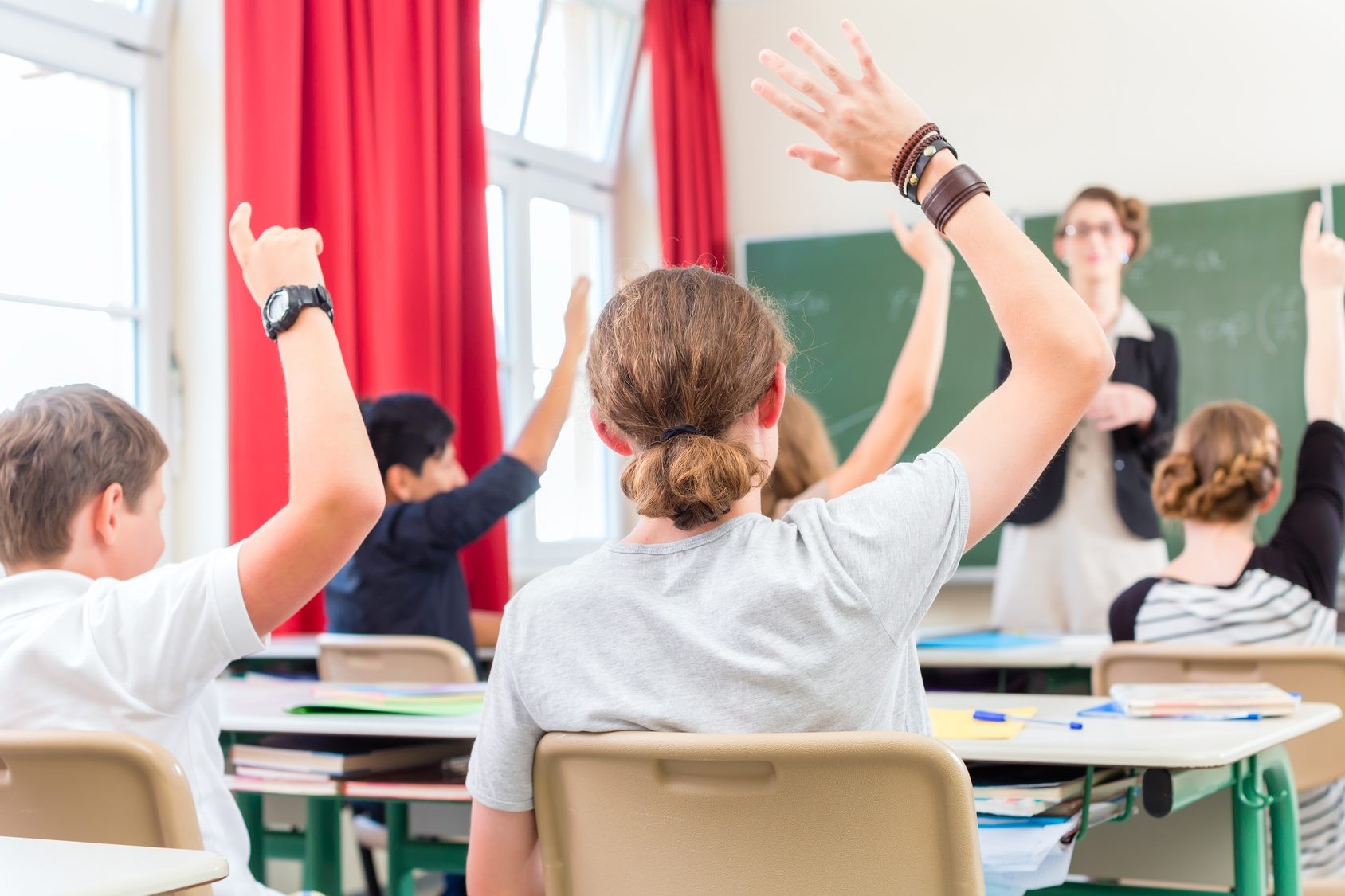 School class teacher giving lesson in front of a blackboard or board teaching students or pupils, they are raising their hands as they know all the answers Lehrer unterrichtet Schler in Klasse einer Schule