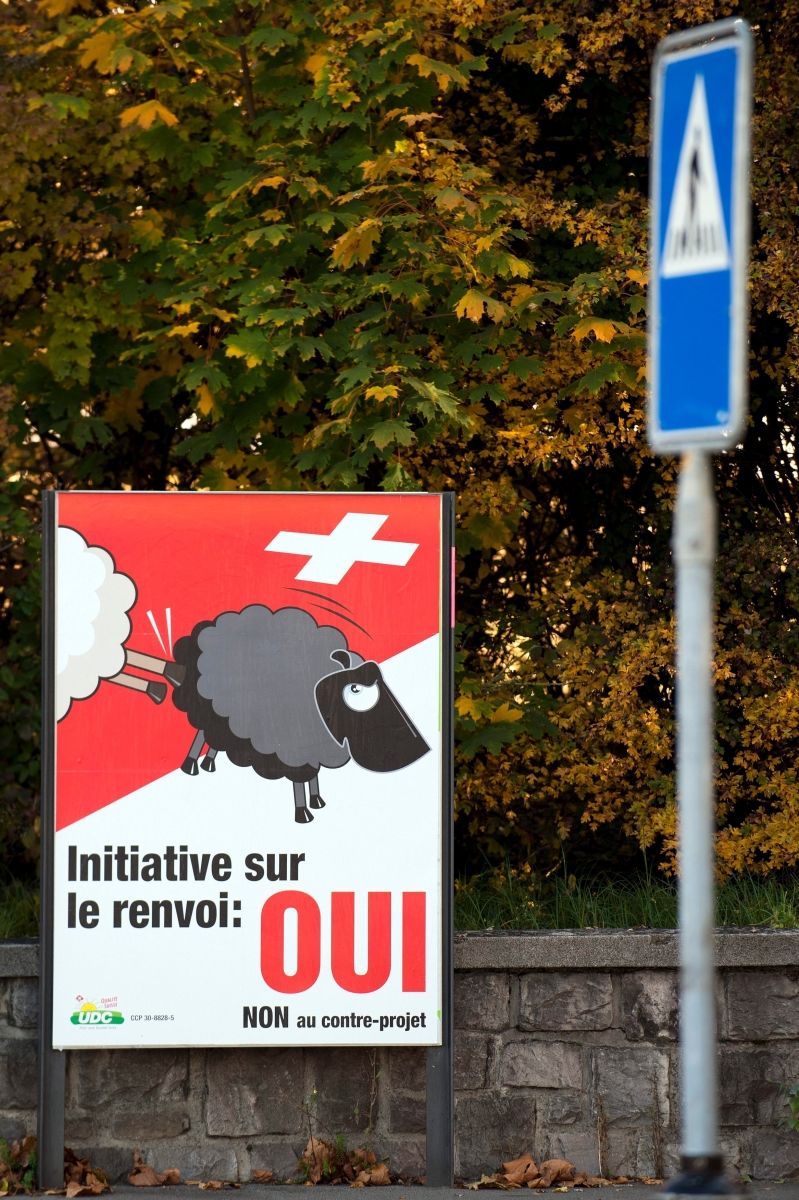 Une affiche de l' Union democratique du centre, UDC, montre un mouton blanc expulsant un mouton noir sur fond de drapeau Suisse et invitant le peuple a voter OUI a l' initiative populaire pour le renvoi des etrangers criminels lors de la votation du 28 novembre prochain photographiee ce jeudi 4 novembre 2010 a Lausanne. (KEYSTONE/Laurent Gillieron) SUISSE UDC VOTATION 28 NOVEMBRE