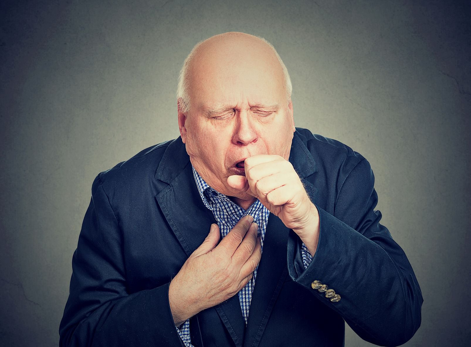 Old man coughing holding fist to mouth isolated on gray background Old man coughing holding fist to mouth