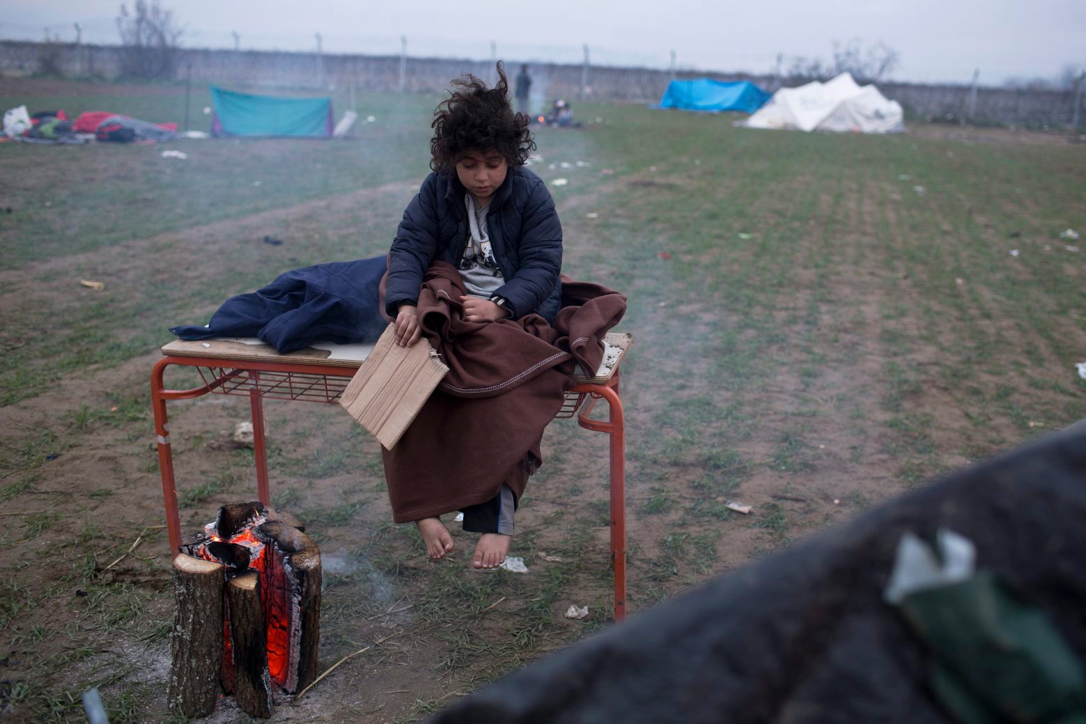 An Iranian child warms near a fire as she wait s to be allowed to cross the Macedonian borders, near the northern Greek village of Idomeni, Friday, Dec. 4, 2015. Macedonian authorities are allowing only people from the war-wracked countries of Syria, Afghanistan and Iraq to cross from Greece on their way to other European Union countries, leading to protests from those from other countries who have been blocking the crossing for all since Wednesday.(AP Photo/Petros Giannakouris) Greece Migrants
