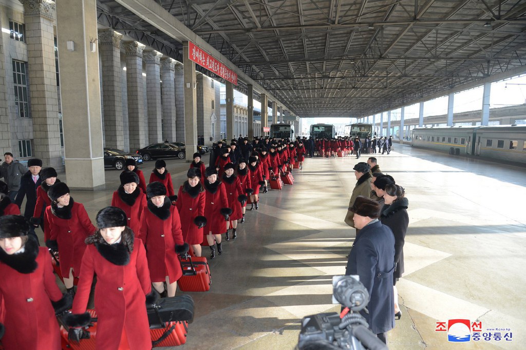 Une photo diffusée par KCNA montre des dizaines de femmes vêtues d'un même manteau d'hiver rouge, portant un chapeau de fourrure brun foncé et une écharpe en fourrure, marchant deux par deux avec une valise rouge dans une gare de Pyongyang.