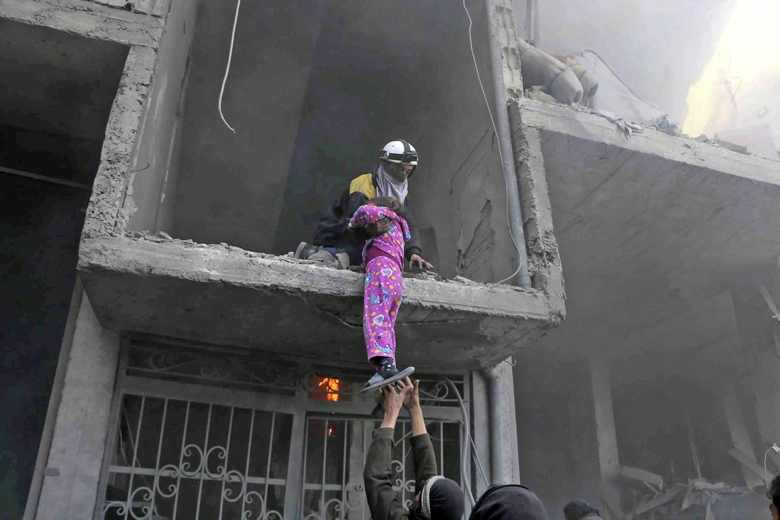 In this photo released on Wednesday Feb. 21, 2018 provided by the Syrian Civil Defense group known as the White Helmets, shows a member of the Syrian Civil Defense group rescuing a young girl from a damaged damaged by airstrikes and shelling by Syrian government forces, in Ghouta, a suburb of Damascus, Syria. New airstrikes and shelling on the besieged, rebel-held suburbs of the Syrian capital killed at least 10 people on Wednesday, a rescue organization and a monitoring group said. (Syrian Civil Defense White Helmets via AP) Syria