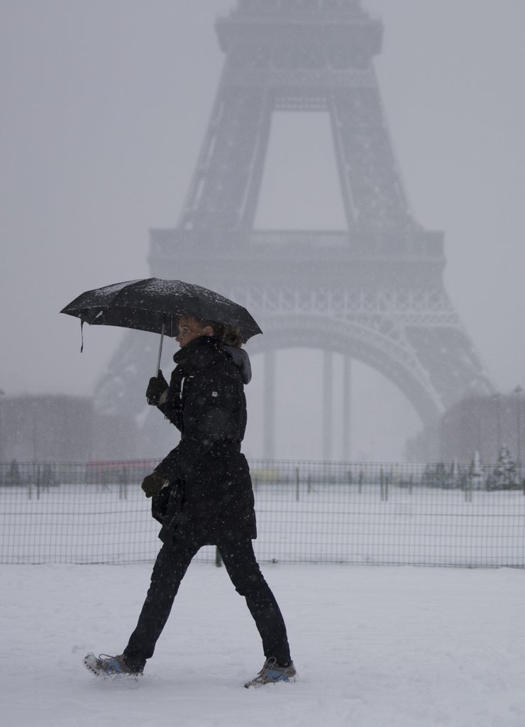 epa03546060 A well-wrapped up woman takes the carpet of snow in her stride as she walks through the snow-covered Champs de Mars park near the Eiffel Tower in Paris, France, 20 January 2013. Heavy snowfall struck Paris, along with several other Western European capitol cities such as London.  EPA/IAN LANGSDON