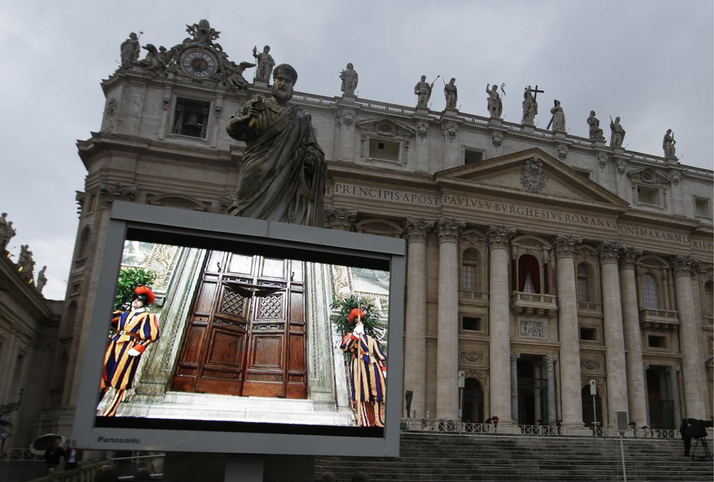 Un écran géant de la place Saint-Pierre montre les portes de la Chapelle Sixtine fermées.