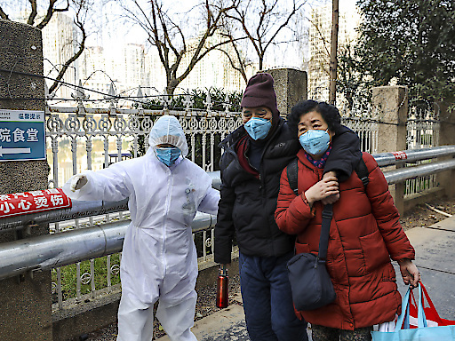 Un membre du personnel médical en combinaison de protection aide un couple à l'extérieur d'un hôpital de Wuhan.